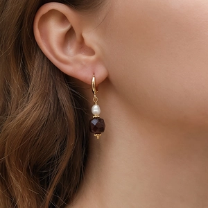 Eleganti orecchini pendenti in oro con perla bianca e gemma rossa su una modella