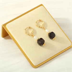 Dettaglio di orecchini dorati con perle bianche e pietre sfaccettate marroni