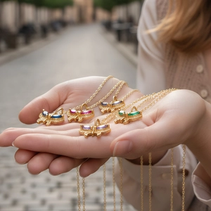 Close-up of butterfly necklaces in gold finish with colorful zircon stones held by a hand