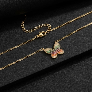 Collar dorado con colgante de mariposa y circonitas de colores sobre fondo de cuero negro