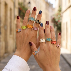 Close-up of bohemian gold leaf rings with colorful enamel worn by a model in outdoor setting