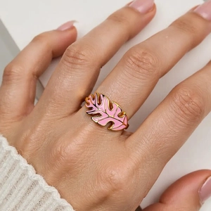 Golden Monstera leaf ring with pink enamel detail shown on finger in a stylish macro view