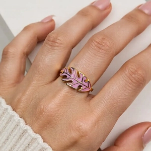 Detail shot of a golden monstera leaf ring with pink enamel worn on a female finger