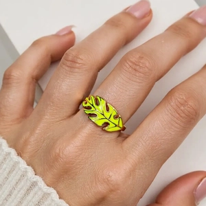 Macro view of a gold monstera leaf ring with vibrant green enamel on a model's finger