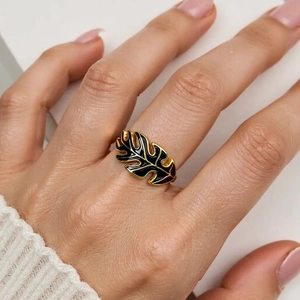 Detail of a gold monstera leaf ring with black enamel drip on a woman's finger