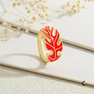 Close-up of golden monstera leaf ring with vibrant red enamel on a white display stand