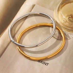 Minimalist 18K gold and silver stainless steel oval bangles displayed on a book
