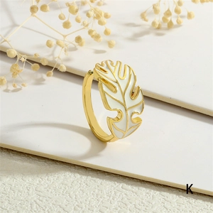 Detail of gold adjustable ring featuring white enamel tropical leaf design on white surface