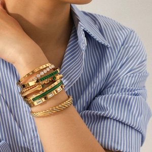 Close-up of stacked 18k gold plated bracelets with zircons and emerald stones on a wrist