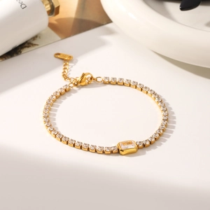 Primer plano de pulsera tenis dorada con circón central rectangular y cierre de langosta