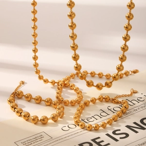 Elegant 18K gold-plated stainless steel bead necklace and bracelet set on a vintage magazine