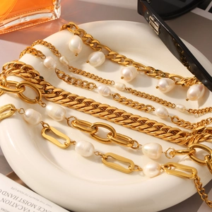 Détail d'une chaîne Figaro dorée et gourmette cubaine avec perles baroques sur plat blanc
