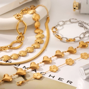 Detailed close-up of 18K gold heart and four-leaf clover necklaces with polished metal shine