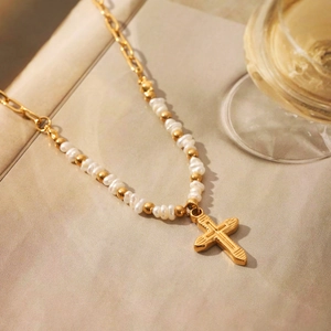 Detailed close-up of a gold cross pendant necklace with pearl beads and metal chain