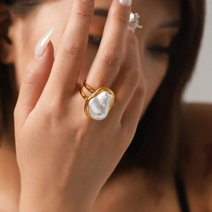 Macro shot of an oversized baroque pearl ring with modern double gold bands on a hand
