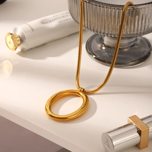 Close-up of golden snake chain necklace with large oval pendant on elegant white surface