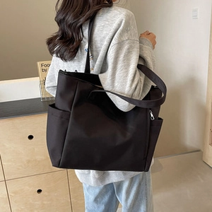 Detail view of a large black tote bag featuring side pockets and reinforced shoulder straps