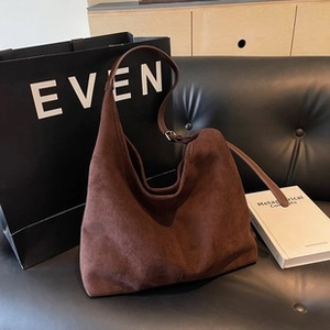 Detailed macro view of brown suede hobo bag texture and adjustable strap on a sofa