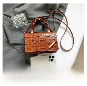 Detail view of brown crocodile texture handbag with pleated handle and metal bar decoration