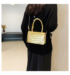 Detail view of gold crocodile embossed handbag with spiral handle and chain strap