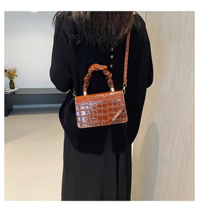 Close-up of dark brown crocodile embossed crossbody bag with ruched handle detail