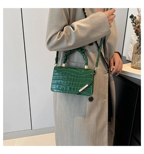 Detail of green crocodile texture handbag with pleated handle and golden metal trim