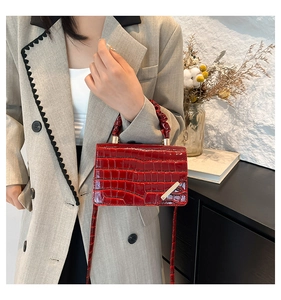 Detail view of red glossy croc-embossed square handbag with unique pleated handle