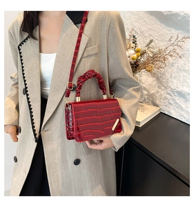 Detail of burgundy crocodile-textured crossbody bag with ruched handle and gold metal trim