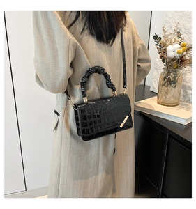 Detail of black glossy crocodile pattern crossbody bag with pleated handle and gold trim