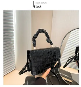 Detail of black crocodile texture handbag with ruched handle and gold metal hardware accents