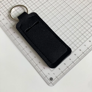 Detail view of black neoprene lipstick holder keychain with metal ring on measuring grid