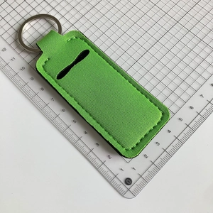 Neon green neoprene lipstick holder keychain with metallic ring measured on a grid