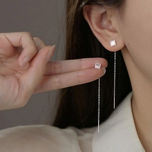 Close-up of long silver chain earrings featuring a sparkling square-cut zircon stone