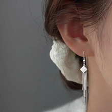Close-up of silver tassel earrings with geometric square stud on ear for women