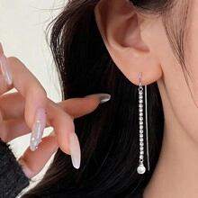 Close-up of long silver linear tassel earrings with rhinestones and white pearl beads