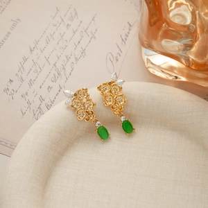 Detail of vintage gold flower earrings with green cat-eye stone on a beige textured plate