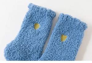 Dettaglio di calze in pile corallo blu con ricamo a cuore giallo e trama soffice