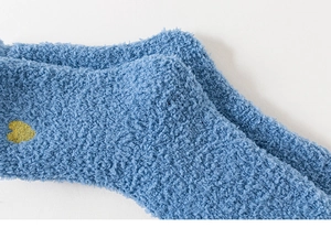 Dettaglio ravvicinato di calze in pile corallo blu con ricamo a cuore giallo e soffice trama