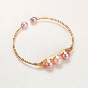 Macro detail of handmade 14K gold-plated wire-wrapped cuff with natural pink pearls