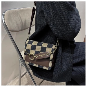 Detail of checkered fabric crossbody bag with leather trim and gold chain ornament