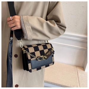 Detail view of woven checkerboard shoulder bag with gold chain and black wide strap