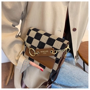 Detail of the checkerboard crossbody bag with leather trim and gold chain on a casual model