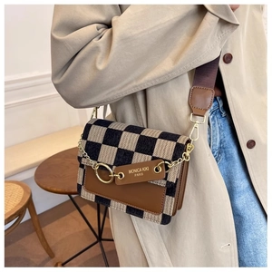 Detail of checkered crossbody bag with gold chain and wide fabric strap on a beige coat