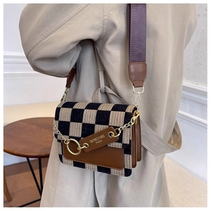 Detail of checkered crossbody bag featuring leather trim and Monica Kiki Paris metal chain tag
