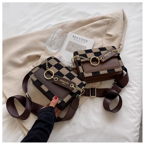 Detail of checkered crossbody bag with brown leather flap and gold ring on beige blazer