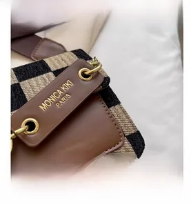 Close-up of checkerboard fabric texture and brown leather flap on a crossbody bag