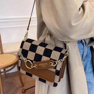 Brown checkerboard crossbody bag with gold chain and leather trim on an elegant outfit