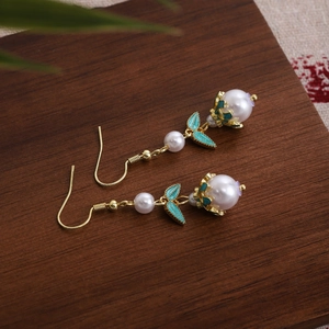 Detail of vintage beaded earrings with green enamel leaves and white pearls on wood