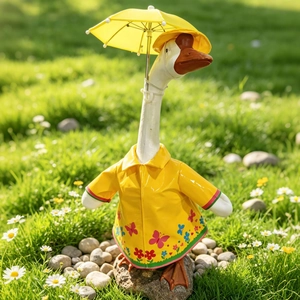 Detail of white garden goose statue wearing a yellow floral raincoat and holding a tiny umbrella