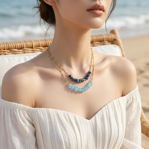 Close-up of double-layer gold necklace with blue tiger eye stone beads on a beach
